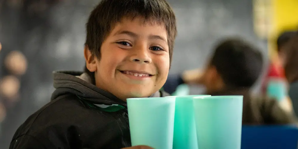 Niño sonriendo con vasos en un comedor